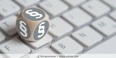 Ein Holzwürfel mit Paragraphen-Symbol liegt auf einer Tastatur.