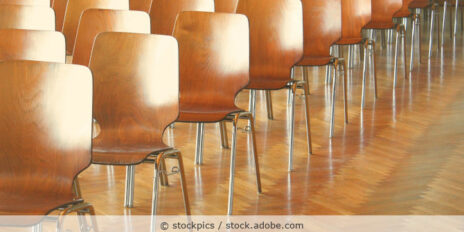 Konferenzstühle aus Holz stehen in Reihen hintereinander in einem Konferenzraum.