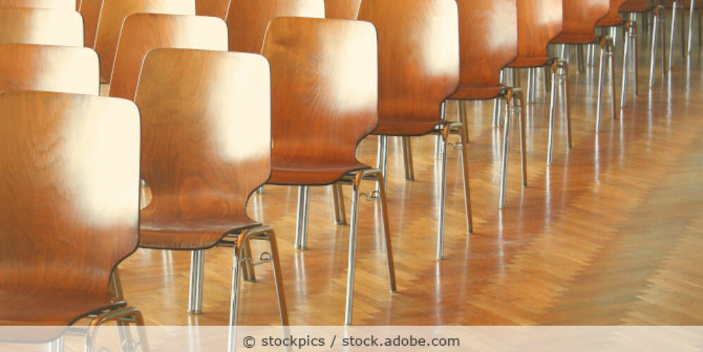 Konferenzstühle aus Holz stehen in Reihen hintereinander in einem Konferenzraum.