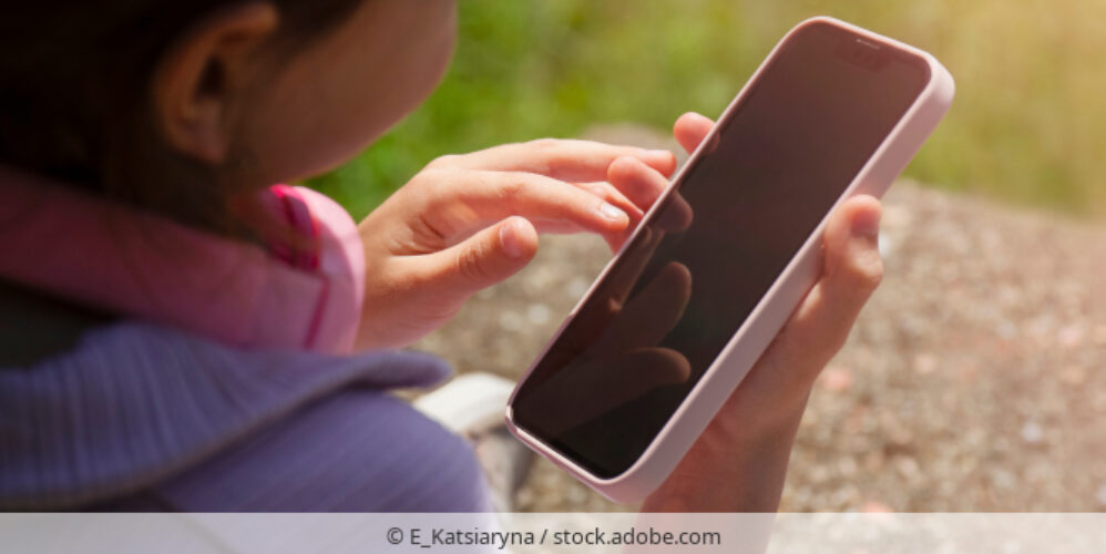 Ein Kind hält ein Smartphone in der Hand und trägt rosa Kopfhörer um den Hals.