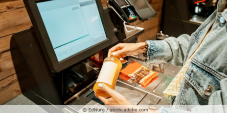 Eine Kundin scannt und bezahlt eine Flasche Saft in einem Supermarkt an einem automatischen Selbstbedienungs-Kassenterminal.