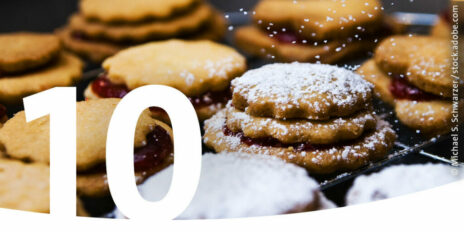 Mit Marmelade gefüllte Plätzchen, auf die gerade Puderzucker gestreut wird als Bild für den 10. Dezember im Adventskalender.