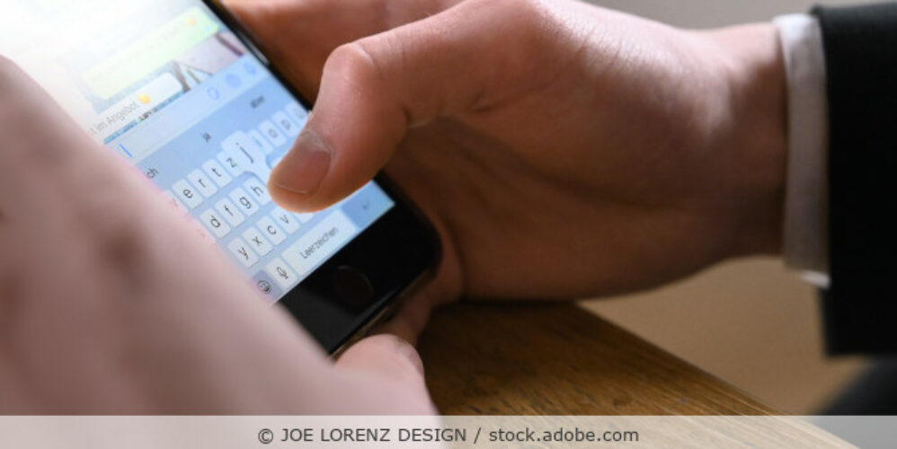 Mann in Business-Kleidung tippt eine Nachricht ins Handy (Chat); Detailaufnahme vom Handy in der Hand.