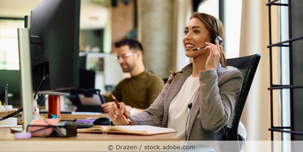 Mitarbeiterin mit Headset sitzt an einem Schreibtisch im Büro und telefoniert.
