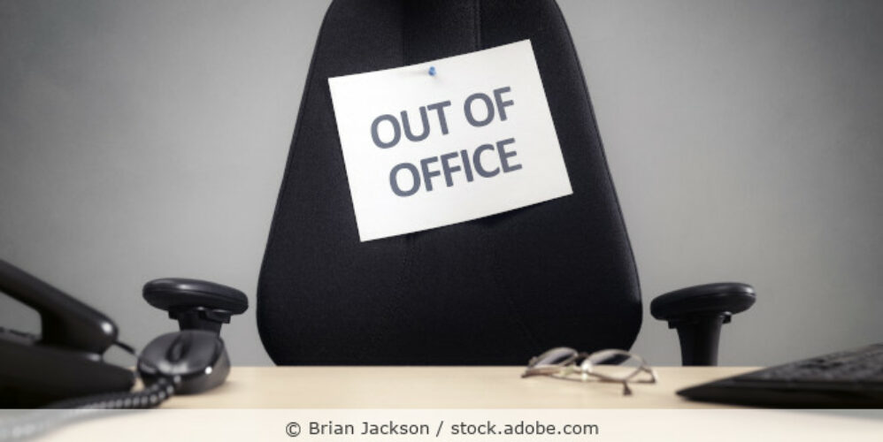 Arbeitsplatz mit Bürostuhl an den ein Zettel mit der Aufschrift „Out of Office“ gepint ist.