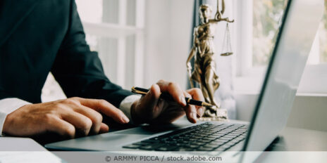 Mann sitzt im Büro und arbeitet an einem Laptop; auf dem Schreibtisch steht eine Justitia-Figur.