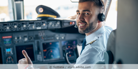 Männlicher Copilot sitzt im Cockpit eines Flugzeugs schaut lächelnd in die Kamera.