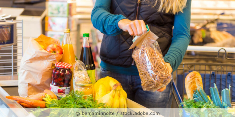 Frau läd Lebensmittel aus einem Einkaufswagen auf das Kassenband in einem Supermarkt.