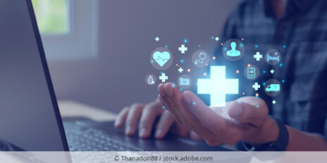 A person sitting in front of a laptop holding icons that symbolize healthcare.