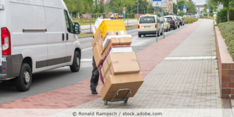 Ein Angestellter eines Paketdienstes liefert Pakete aus, die Pakete werden auch einer Sackkarre gestapelt transportiert.