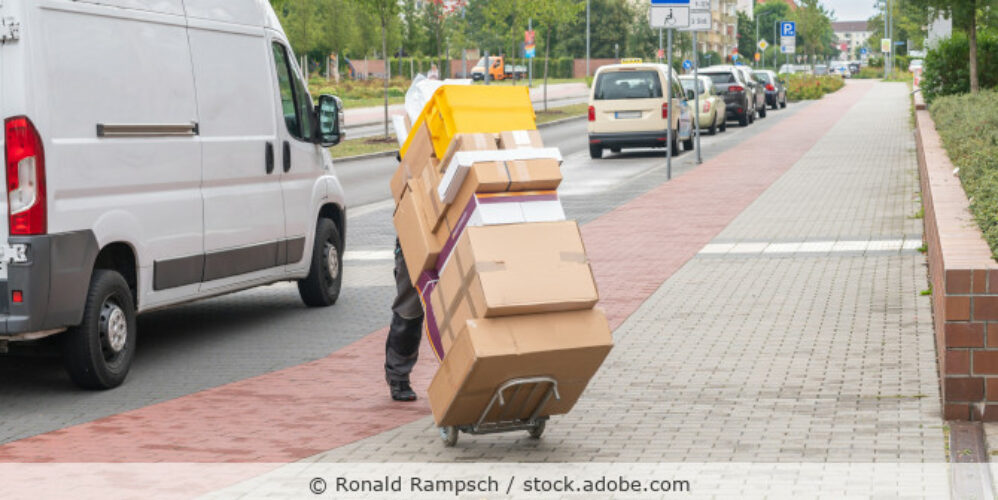 Ein Angestellter eines Paketdienstes liefert Pakete aus, die Pakete werden auch einer Sackkarre gestapelt transportiert.
