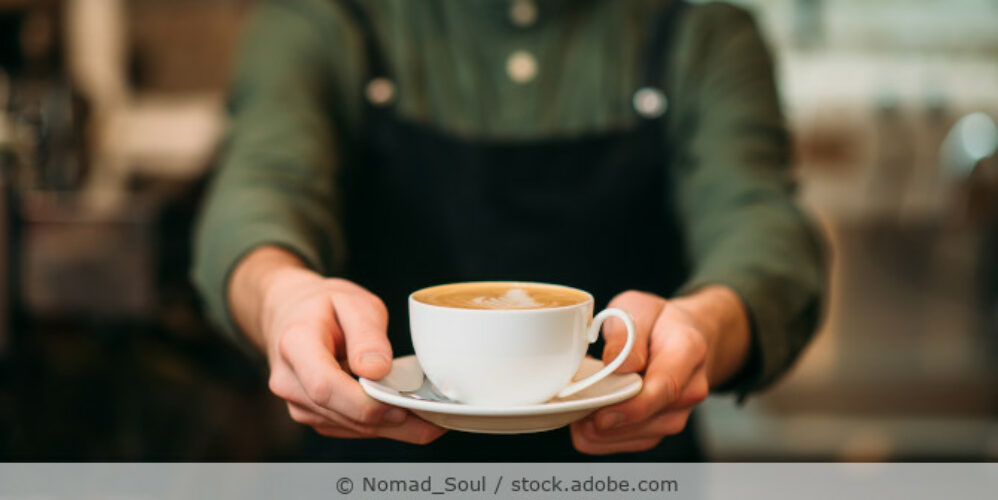 Ein Kellner reicht eine Tasse Cappuchino.