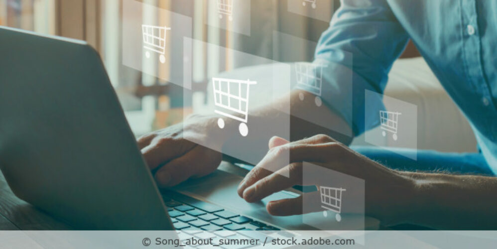 Ein Mann sitzt an einem Laptop, im Vordergrund sind Einkaufswagen-Icons als Illustration zu sehen.