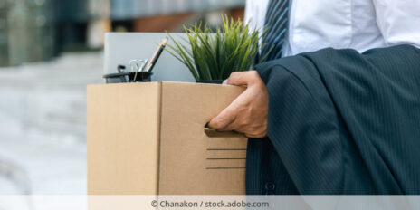 Mann verlässt Bürogebäude mit persönlichen Gegenständen in einem Karton.