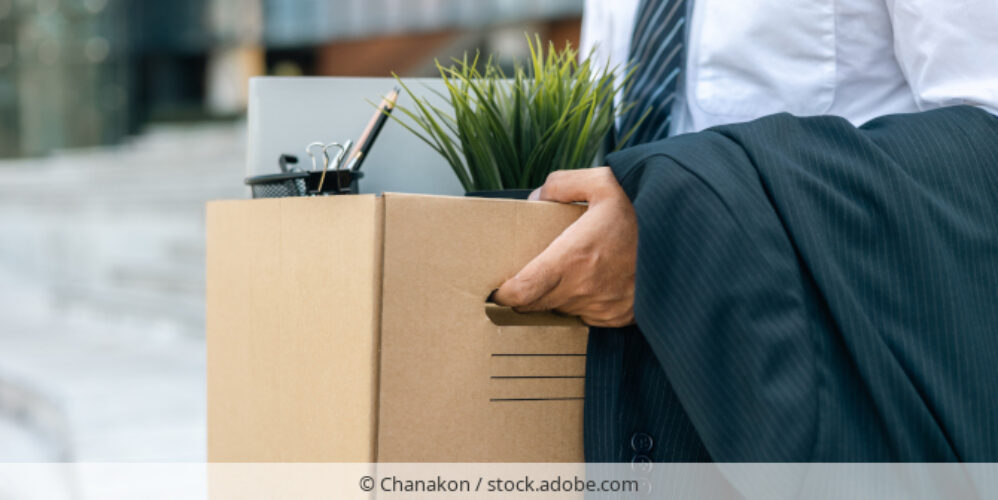Mann verlässt Bürogebäude mit persönlichen Gegenständen in einem Karton.