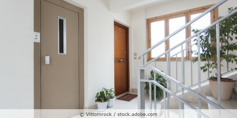Hausflur eines Mehrfamilienhaus mit Blick auf die Treppe, eine Wohnungstür und die Fahrstuhltür.