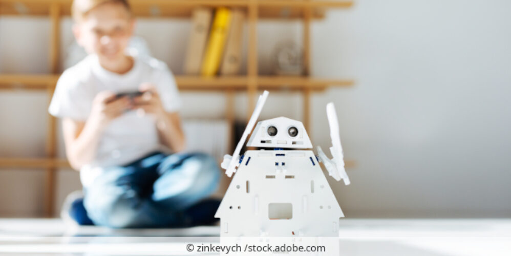 Kind sitzt auf Boden und steuert Roboter-Spielzeug.