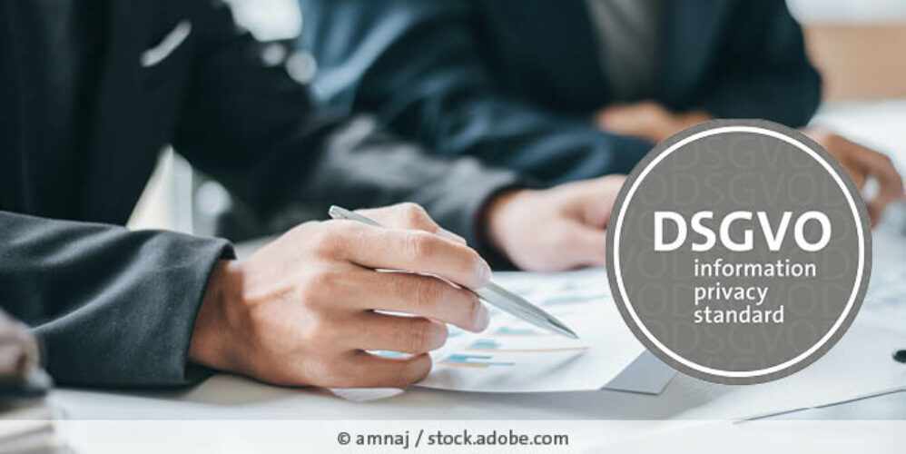 Mann im Anzug sitzt am Tisch und hält ein Dokument in der Hand, rechts ist das „DSGVO – information privacy standard“-Logo zu sehen.