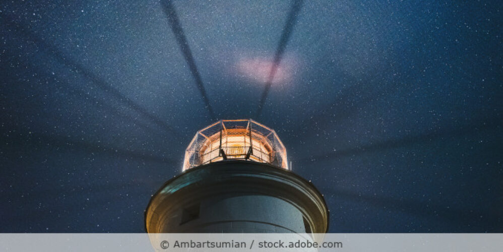 Leuchtturm, dessen Licht den dunklen Nachthimmel erhellt.