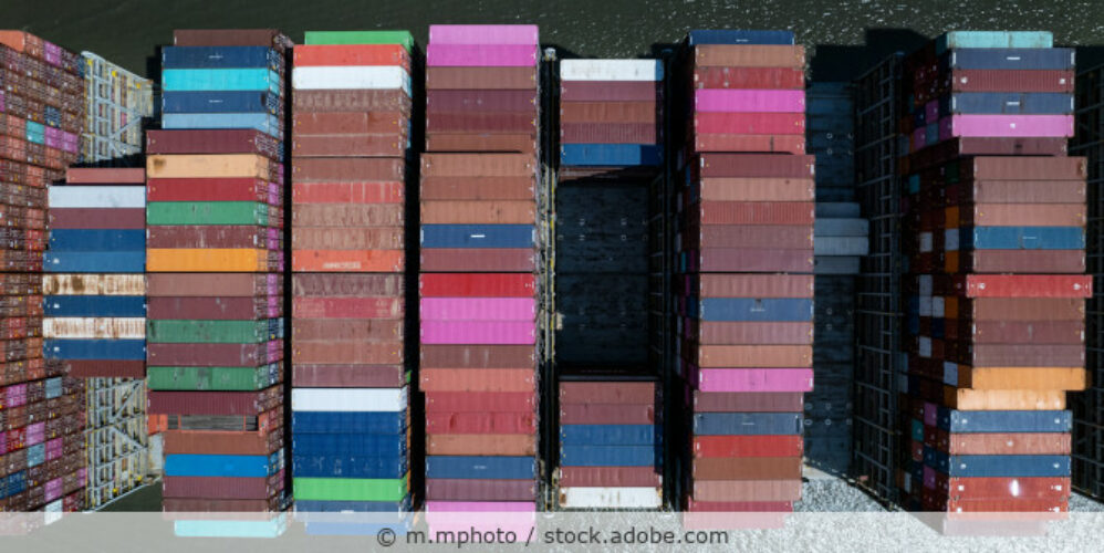 Fahrendes Containerschiff beladen mit Containern in unterschiedlichen Farben von oben fotografiert.