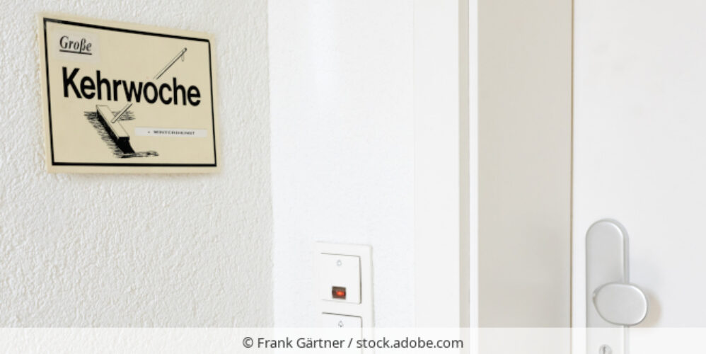 Ein Schild mit der Aufschrift "Große Kehrwoche" hängt neben einer Wohungstür.