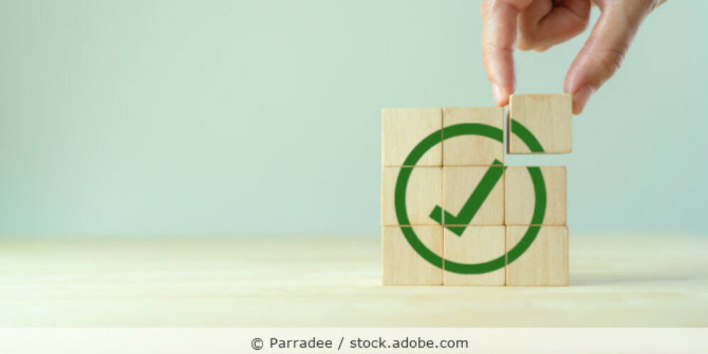 Quadrat aus Holzwürfeln auf denen ein Check-Haken abgebildet ist.