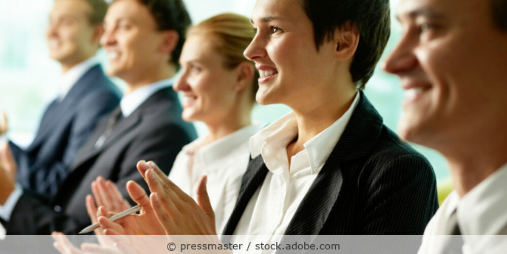 Eine Gruppe von Männern und Frauen in Businesskleidung ist nebeneinander und klatschen Beifall.