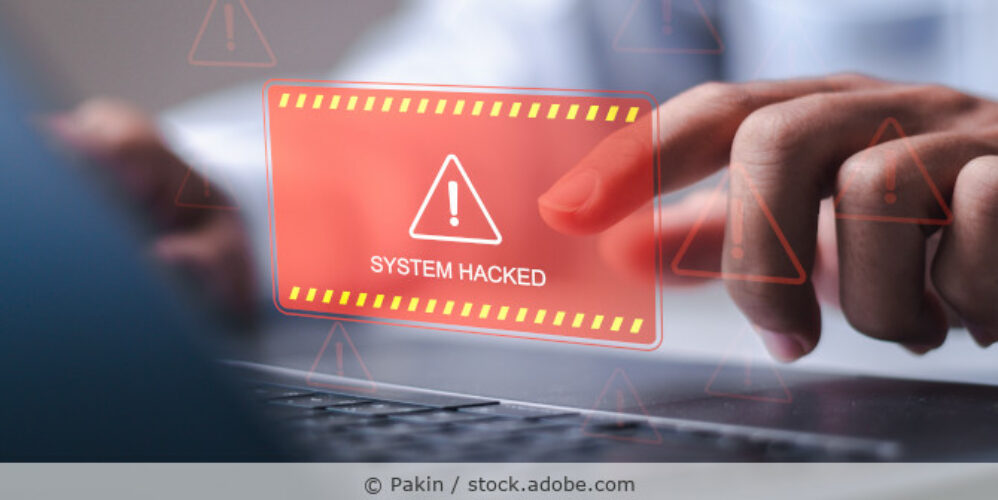Ein Mann sitzt am Laptop, im Vordergrund ist einen Illustration mit rotem Warndreieck und dem Hinweis „System Hacked“ zu sehen.