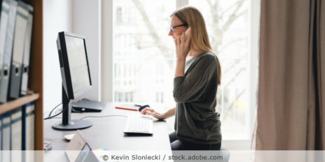 Eine Frau arbeitet im Homeoffice an ihrem Laptop und telefoniert.