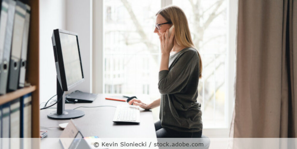 Eine Frau arbeitet im Homeoffice an ihrem Laptop und telefoniert.