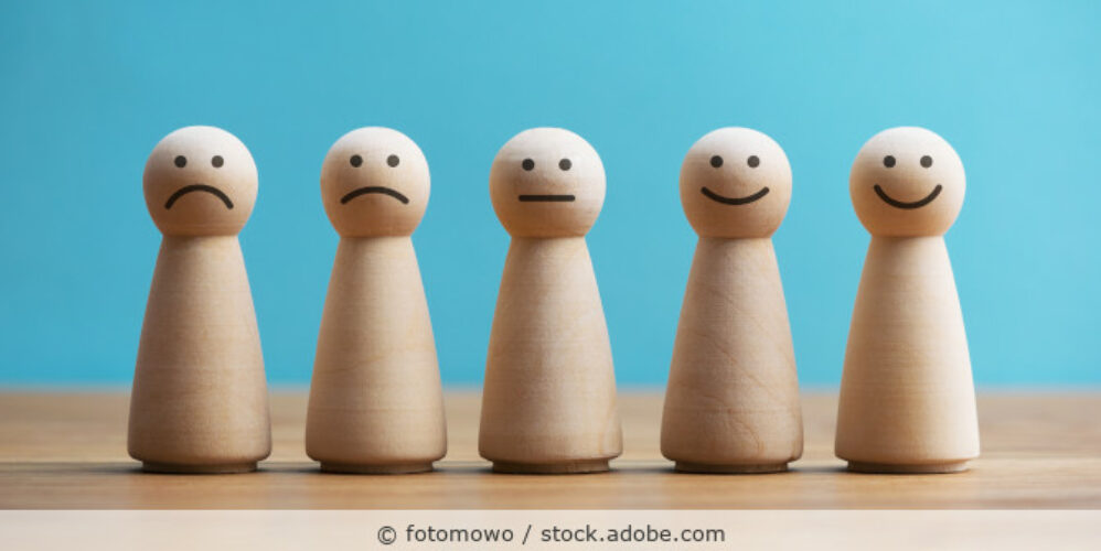 Fünf Holzspielfiguren stehen als Skala nebeneinander mit unterschiedlichen Gesichtsausdrücken – von unzufrieden bis zufrieden.