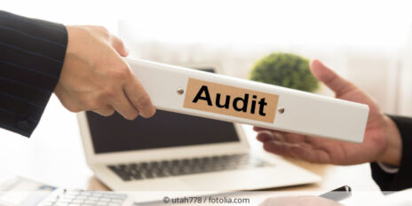 Person überreicht jemandem weißen Ordner mit der Aufschrift Audit.