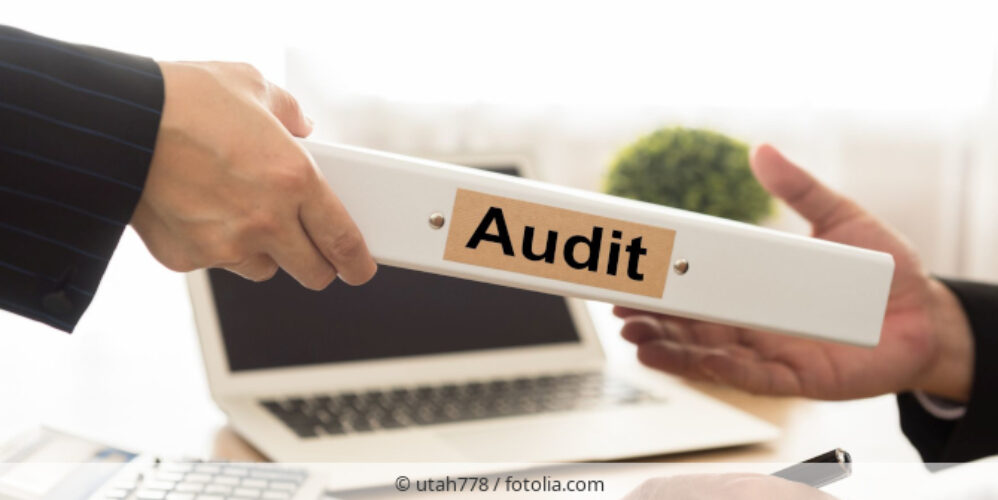 Person überreicht jemandem weißen Ordner mit der Aufschrift Audit.