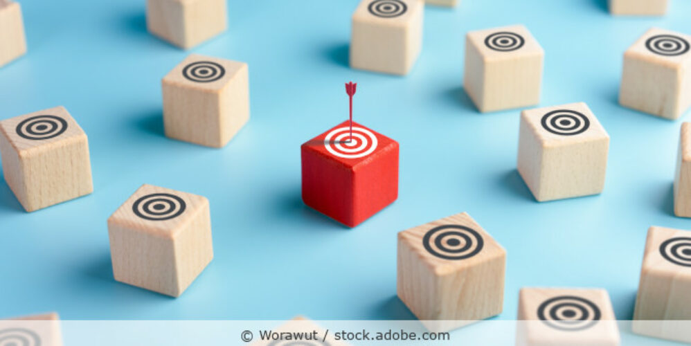 Holzklötze mit Zielscheiben und auf dem Klötzchen in der Bildmitte steckt ein roter Pfeil.