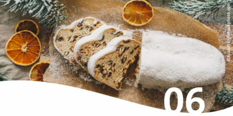Angeschnittener Christstollen auf dekorativem Holzbrett im Vordergrund die Zahl 6