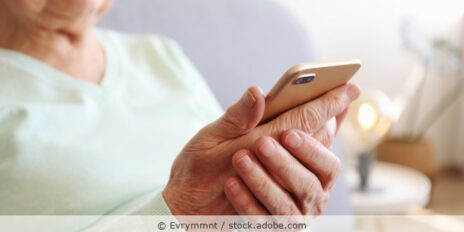 Eine ältere Frau hält ein Handy in den Händen und schaut aufs Display.