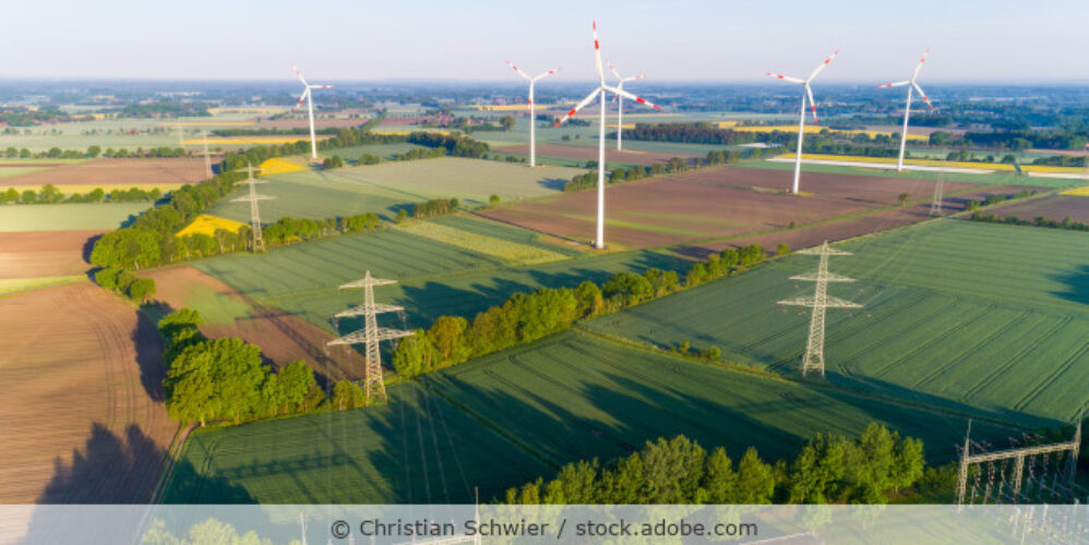 Blick auf Windräder und Strommasten, die auf Feldern stehen.