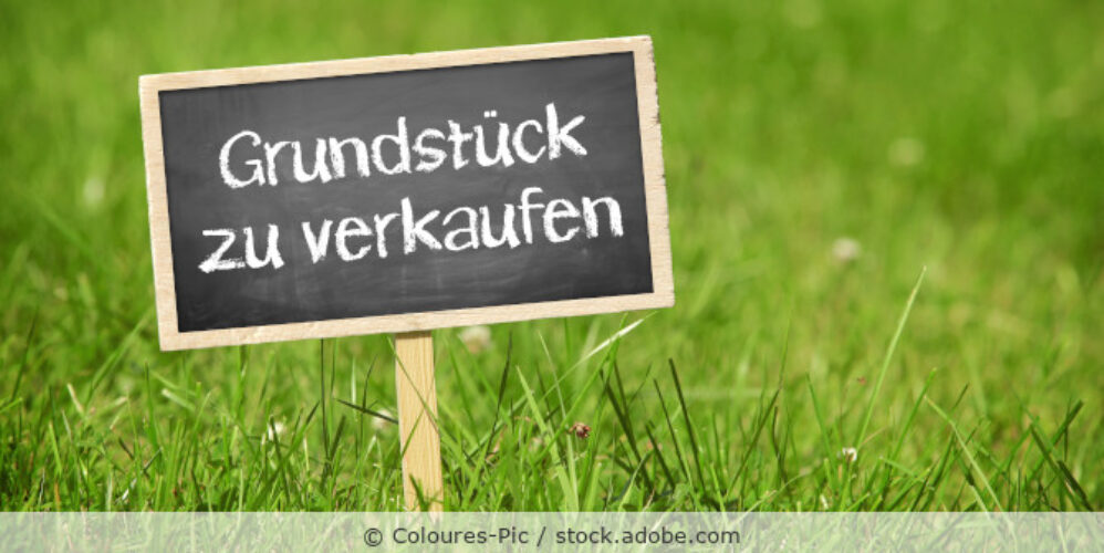 Ein Schild mit der Aufschrift Grundstück zu verkaufen steht auf einer Wiese.