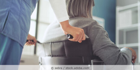 Pflegerin schiebt eine grauhaarig Patientin im Rollstuhl.