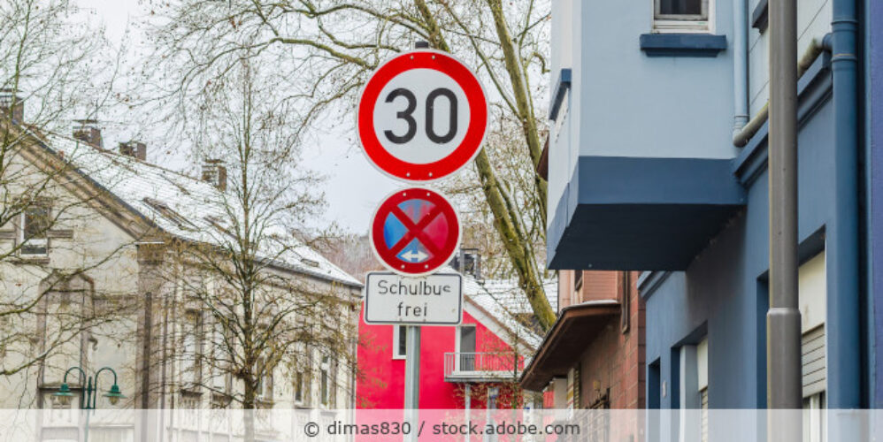 Ein Mast mit drei Schildern (Tempo 30, Halteverbot, Schulbus frei) steht an einer Straße im Wohngebiet.
