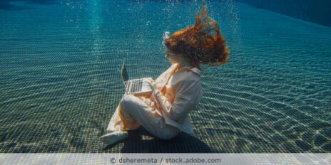 Eine Frau in Businesskleidung arbeitet am Laptop unter Wasser.