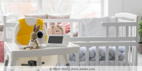 Babyphone mit Spielzeug auf einem Hochstuhl vor einem Kinderbett.