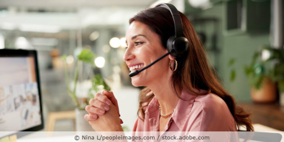 Eine Frau mit Headset an ihrem Schreibtisch im Gespräch.